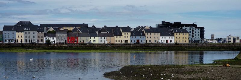 Buildings by river against sky