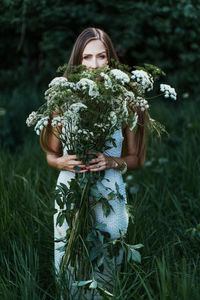 Midsection of woman holding flowering plant on field