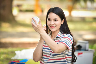 Smiling woman applying make-up at park