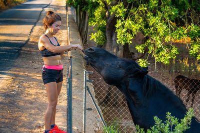 Side view of woman standing by tree and horse