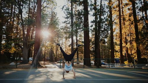 Full length of man practicing handstand on road against trees