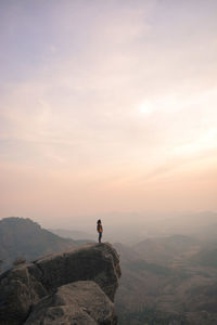 Young man standing on mountain against sky during sunset