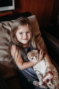 Portrait of cute girl with cat sitting on chair at home