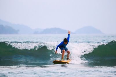 Full length of boy surfing on sea against sky