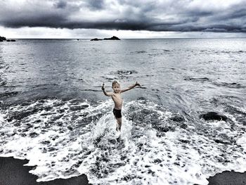 Boy playing on shore at beach against cloudy sky