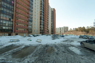 Snow covered road by buildings against sky in city