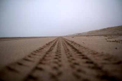 Tire tracks on sand dune against clear sky