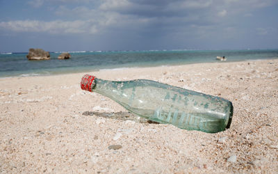 Abandoned bottle on shore at beach against sky