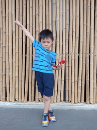 Full length of boy holding mobile phone while standing against bamboos