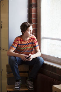 Thoughtful boy looking out through window in locker room at school