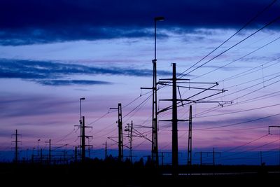 Silhouette electricity pylons against sky during dusk