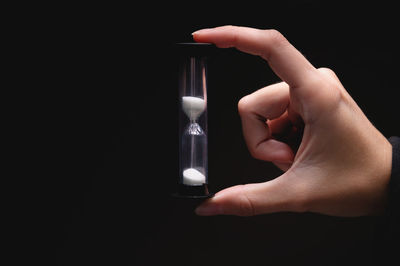 Cropped hand holding hourglass against black background