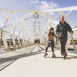 Full length of father holding daughter roller skating on footbridge