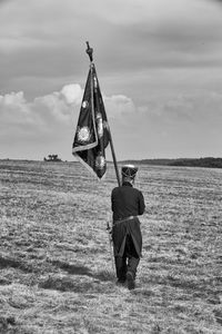 Rear view full length of man with flag walking on field against sky