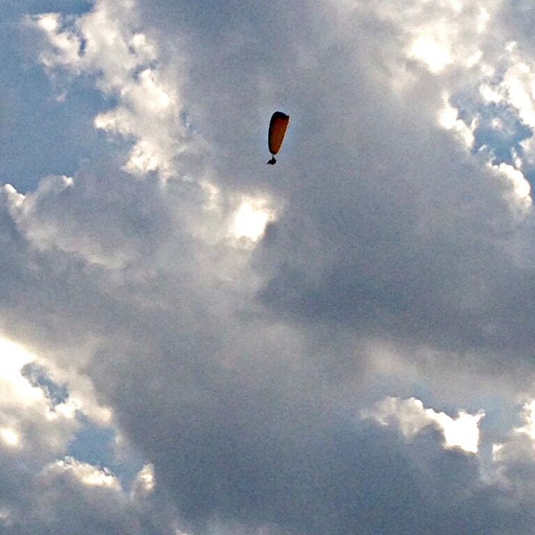 flying, low angle view, mid-air, sky, cloud - sky, scenics, beauty in nature, tranquility, cloud, nature, parachute, paragliding, hot air balloon, tranquil scene, freedom, adventure, cloudy, outdoors, blue, transportation