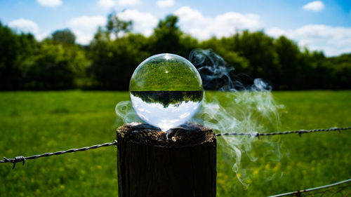 Close-up of crystal ball on wooden post on field