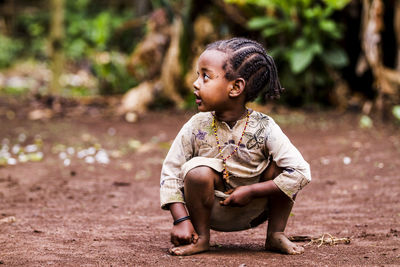 Cute girl looking away while crouching outdoors