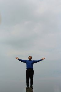 Young man with arms outstretched standing on cliff against sky