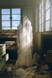 Woman in wedding dress standing by window in abandoned room