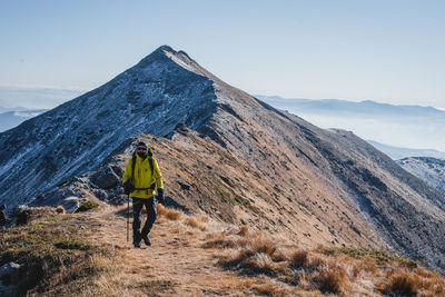 Rear view of man walking on mountain against sky