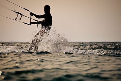 Side view of man kiteboarding on sea against clear sky during sunset