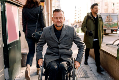 Disabled mature man looking away while sitting on wheelchair in city