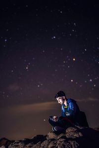 Young man sitting on land against sky at night