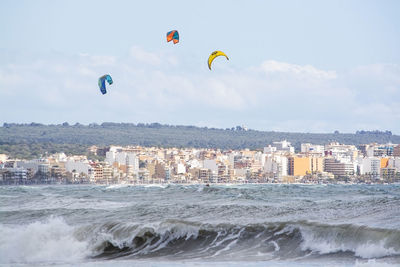 People in sea by cityscape against sky