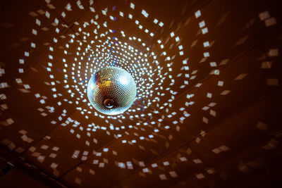 Low angle view of illuminated disco ball hanging from ceiling in nightclub