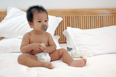 A little kid sitting on white bed sheets