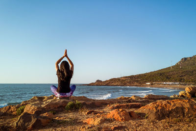 Rear view of woman standing on rock in sea against clear sky