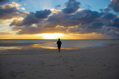 Rear view of man running at beach against sky during sunset