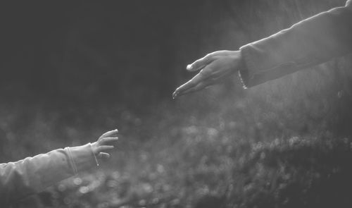 Cropped hand of mother reaching towards daughter in park