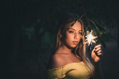 Young woman holding lit sparkler at night
