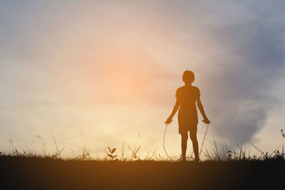 Silhouette girl skipping on field against sky during sunset
