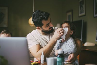 Father blowing nose of son in living room