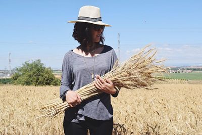 Young woman holding wheat crops on field against sky