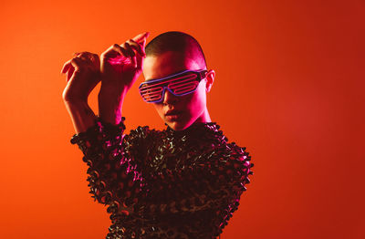 Young woman with shaved head wearing novelty glasses against orange background