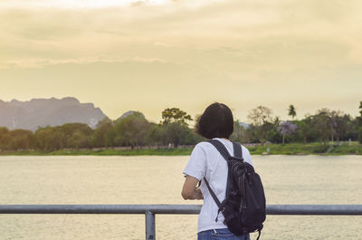 Rear view of woman standing by railing against sky