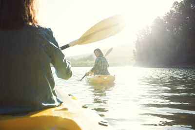 Rear view of female friends kayaking on lake against sky during sunny day