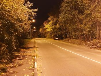 Illuminated road by trees in city at night