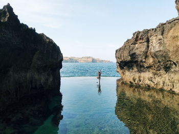 Man standing on rock by sea against sky