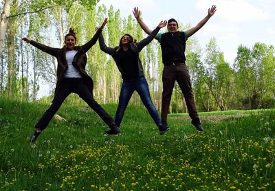 Happy friends jumping on grassy field at park