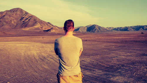 Rear view of man standing on barren landscape against sky