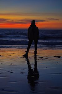 Silhouette woman standing at beach against sky during sunset