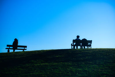 Rear view of people walking on field against clear sky
