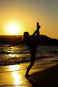 Side view of silhouette man climbing on beach against sky during sunset