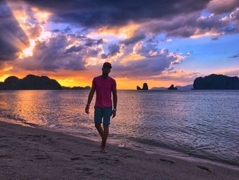 Rear view of man on beach against sky during sunset