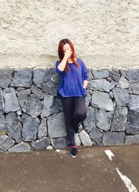 Woman covering her face with hand while leaning on stone wall