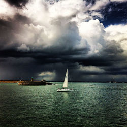 Sailboat sailing in sea against cloudy sky